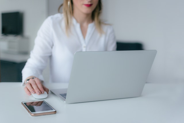 Person in white sitting at a white desk working on a laptop with an exterior mouse